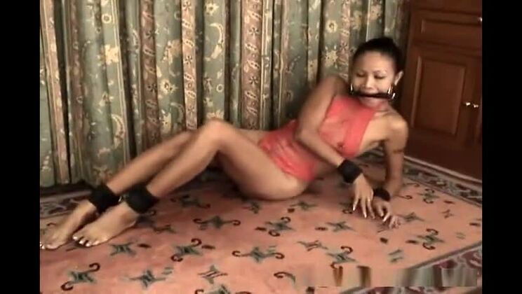 Chica asiática delgada en lencería roja esposada y amordazada